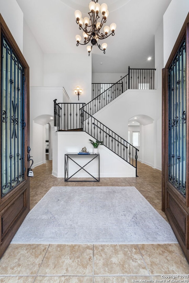 foyer featuring arched walkways, a towering ceiling, an inviting chandelier, and stairs