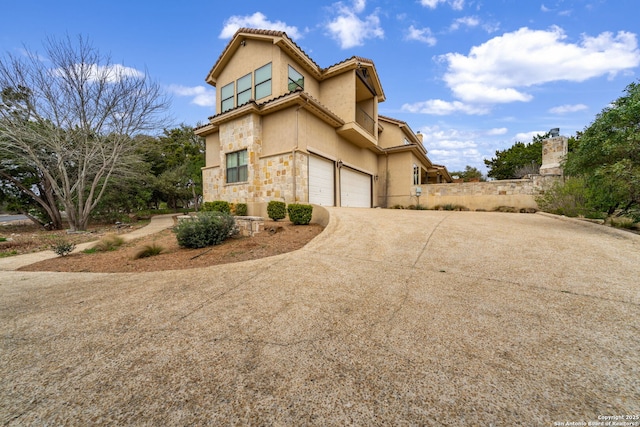 exterior space with a garage, stone siding, driveway, and stucco siding