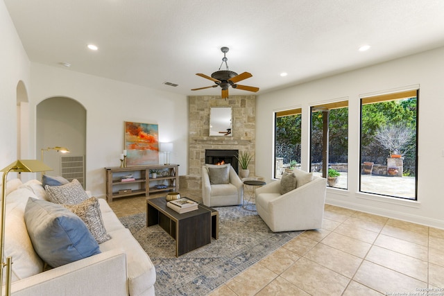 living room with light tile patterned floors, arched walkways, a stone fireplace, recessed lighting, and visible vents