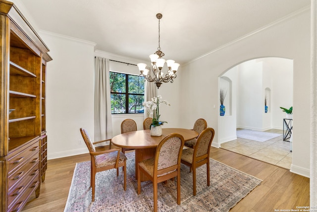 dining room featuring baseboards, arched walkways, wood finished floors, crown molding, and a notable chandelier