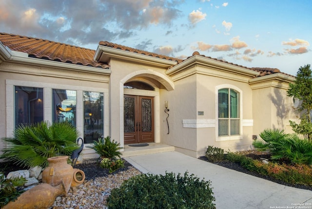 view of exterior entry with stucco siding, a tile roof, and french doors