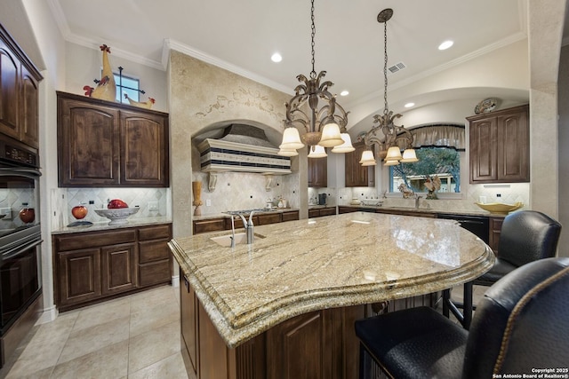 kitchen featuring visible vents, hanging light fixtures, dark brown cabinets, light stone countertops, and an island with sink