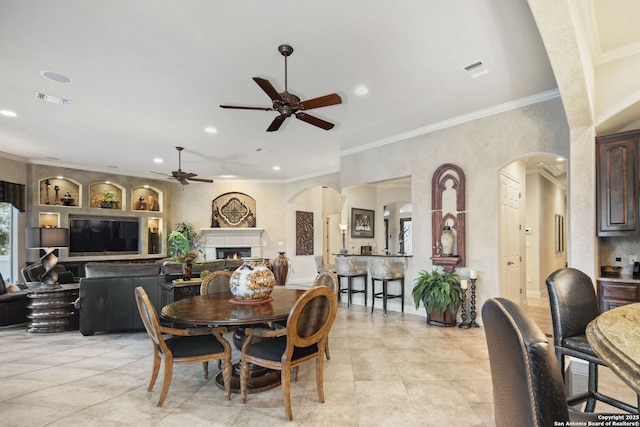 dining area with a warm lit fireplace, visible vents, arched walkways, and crown molding