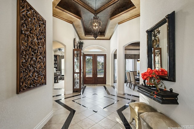 entryway with arched walkways, ornamental molding, a raised ceiling, and baseboards