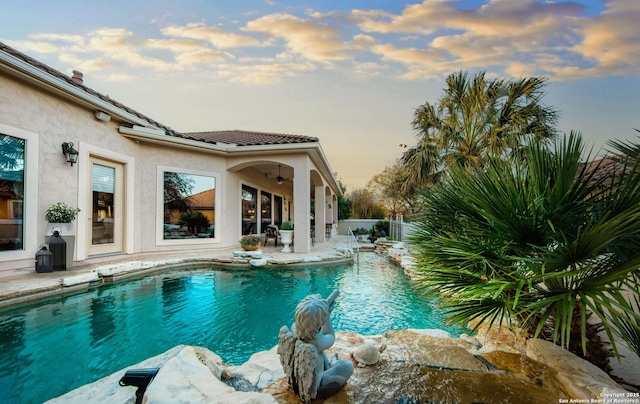 pool at dusk featuring a patio area, a ceiling fan, and a fenced in pool