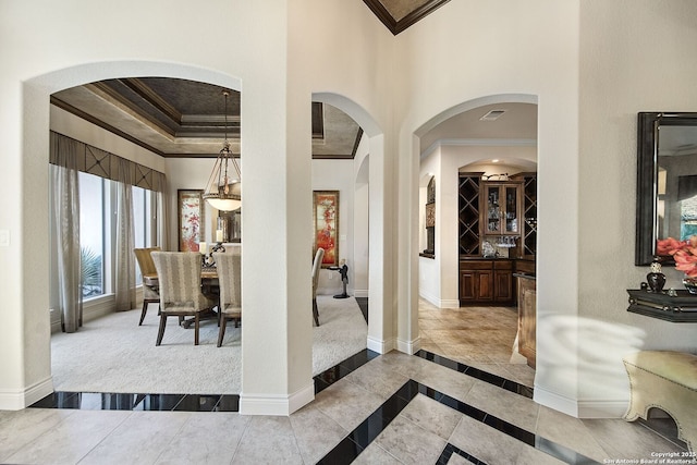 entryway with a tray ceiling, visible vents, a towering ceiling, ornamental molding, and baseboards