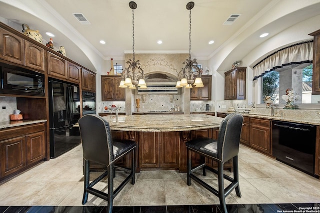 kitchen featuring black appliances, a kitchen bar, visible vents, and light stone counters