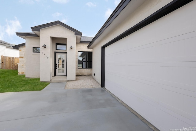 property entrance with stone siding, concrete driveway, a lawn, stucco siding, and a patio area