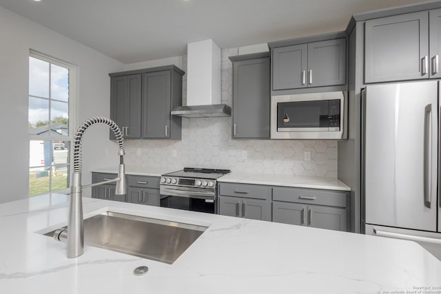 kitchen with wall chimney exhaust hood, appliances with stainless steel finishes, a sink, and gray cabinetry