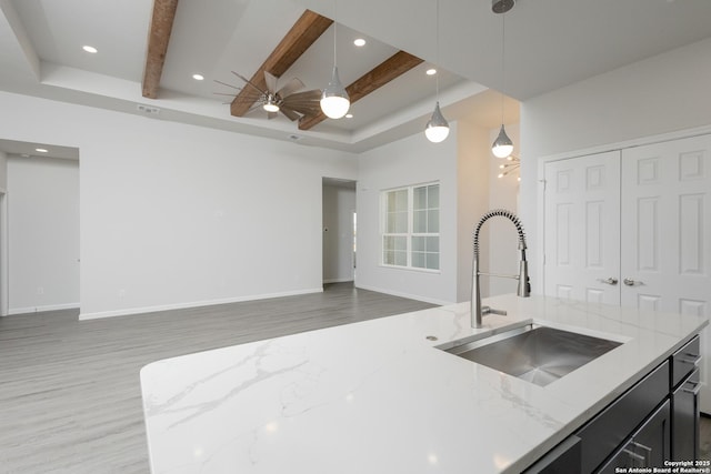 kitchen featuring light stone counters, wood finished floors, beamed ceiling, decorative light fixtures, and a sink