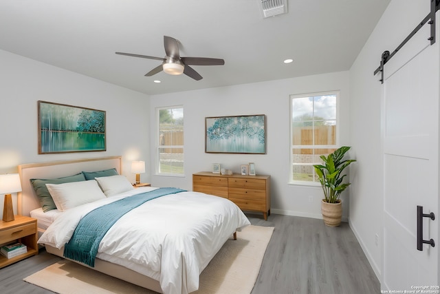 bedroom with a barn door, visible vents, baseboards, light wood-type flooring, and recessed lighting