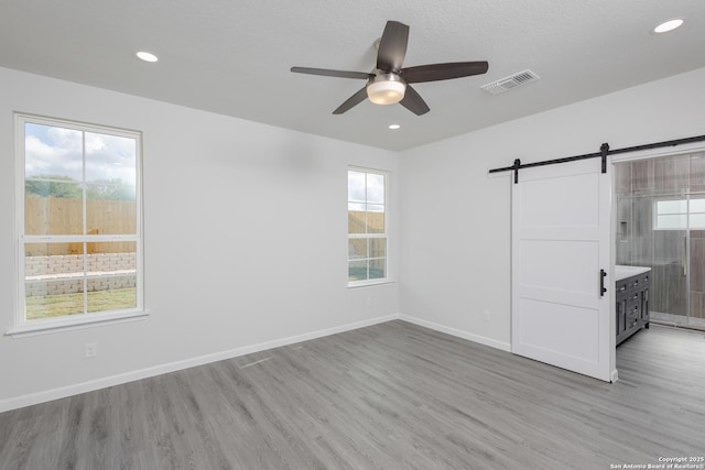 unfurnished bedroom featuring a barn door, light wood-style flooring, visible vents, and baseboards