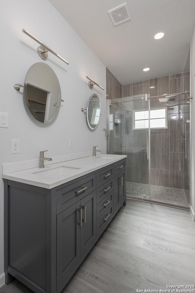 bathroom featuring double vanity, a shower stall, visible vents, and a sink