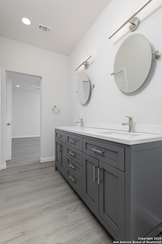 bathroom featuring double vanity, visible vents, a sink, wood finished floors, and baseboards