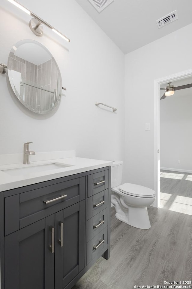 full bath featuring toilet, vanity, wood finished floors, and visible vents