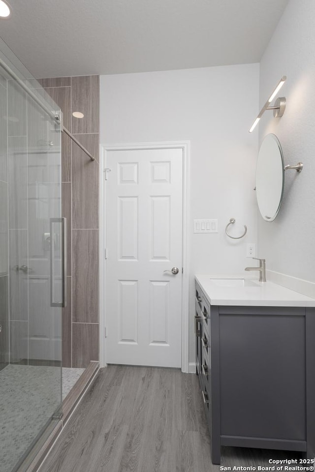 full bath featuring a tile shower, wood finished floors, and vanity