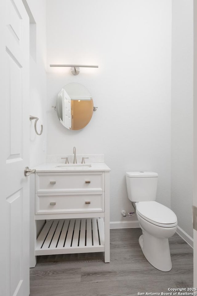 half bathroom featuring toilet, baseboards, wood finished floors, and vanity