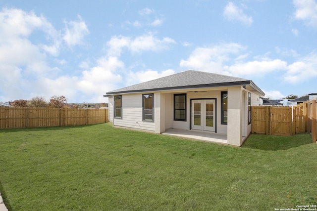 rear view of house with a lawn, a fenced backyard, roof with shingles, french doors, and a patio area