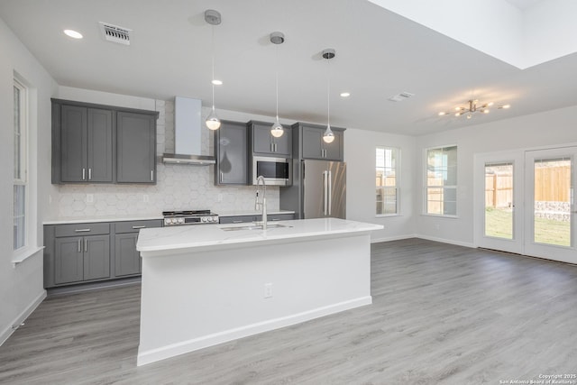 kitchen with a sink, visible vents, wall chimney range hood, appliances with stainless steel finishes, and pendant lighting