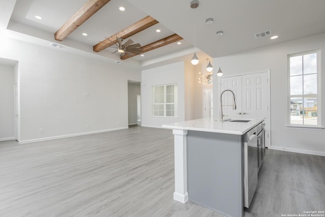 kitchen featuring a kitchen island with sink, a sink, open floor plan, light countertops, and pendant lighting