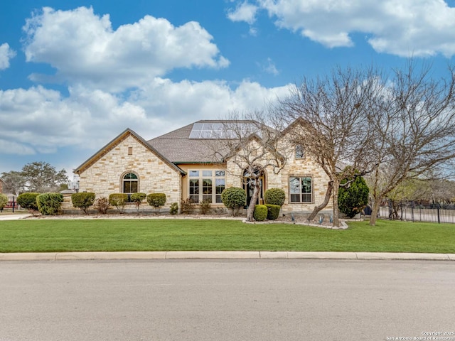 french country style house featuring stone siding, a front yard, and roof mounted solar panels