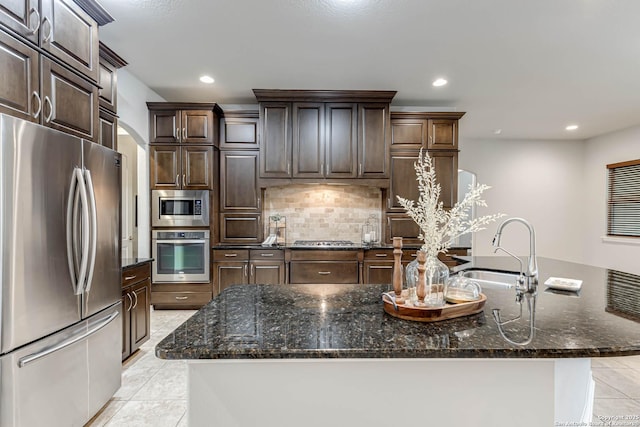 kitchen featuring a center island with sink, light tile patterned floors, appliances with stainless steel finishes, a sink, and dark brown cabinets