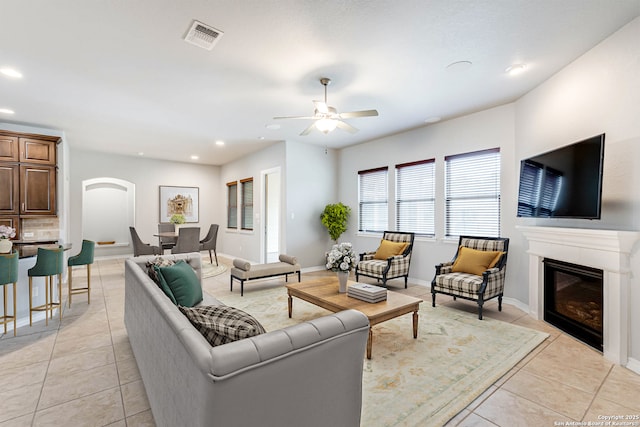 living area featuring light tile patterned floors, visible vents, baseboards, a glass covered fireplace, and recessed lighting