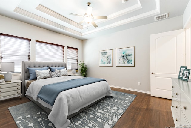 bedroom featuring baseboards, visible vents, dark wood-style flooring, a tray ceiling, and crown molding