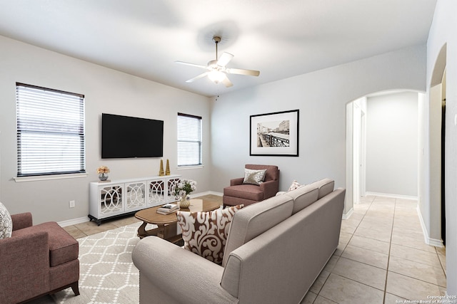 living area with light tile patterned floors, baseboards, arched walkways, and a ceiling fan