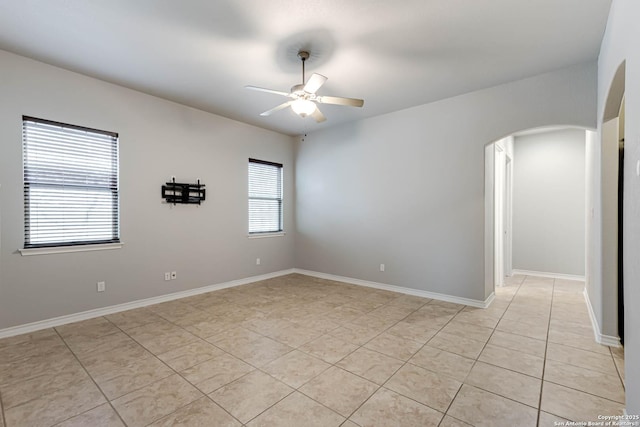 unfurnished room with a ceiling fan, arched walkways, baseboards, and light tile patterned floors