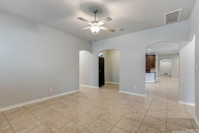 unfurnished room featuring arched walkways, light tile patterned floors, visible vents, and a ceiling fan