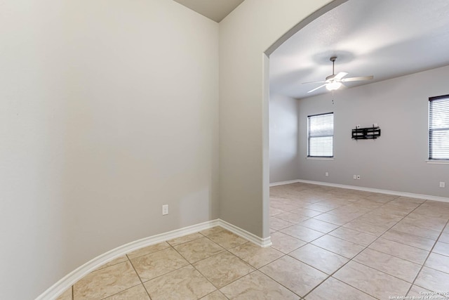 empty room featuring arched walkways, light tile patterned floors, a ceiling fan, and baseboards