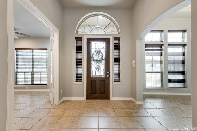 foyer entrance with arched walkways, light tile patterned floors, and baseboards