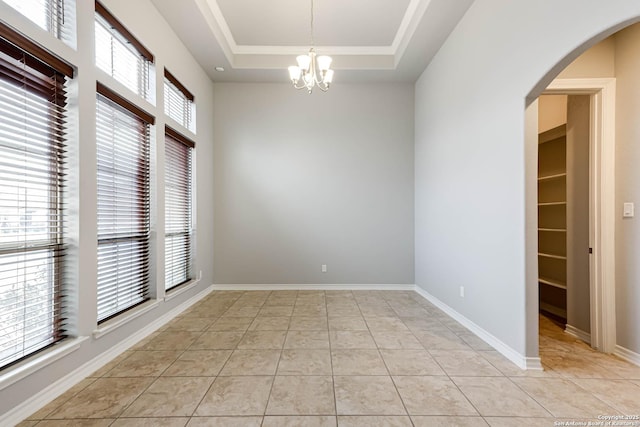 spare room featuring light tile patterned floors, baseboards, arched walkways, and a tray ceiling