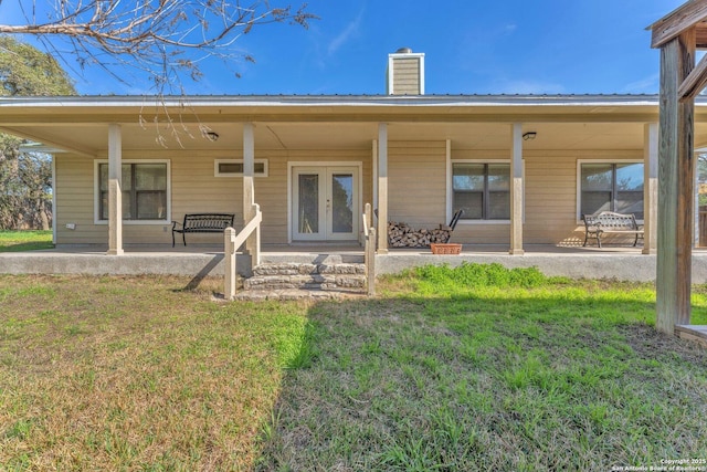 rear view of property with metal roof, french doors, a chimney, and a lawn