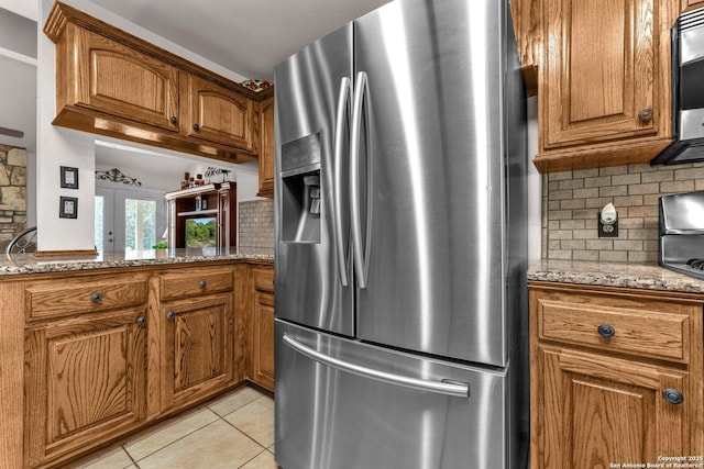 kitchen with light tile patterned floors, brown cabinetry, light stone counters, stainless steel appliances, and backsplash