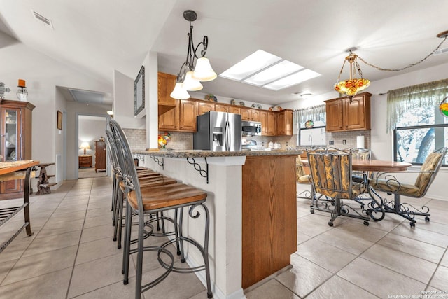 kitchen with stainless steel appliances, visible vents, hanging light fixtures, brown cabinets, and dark countertops