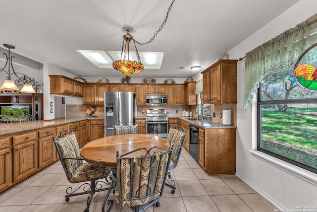 kitchen with light stone counters, stainless steel appliances, hanging light fixtures, brown cabinetry, and a sink