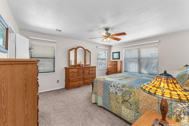 bedroom with a textured ceiling, light colored carpet, visible vents, baseboards, and a ceiling fan