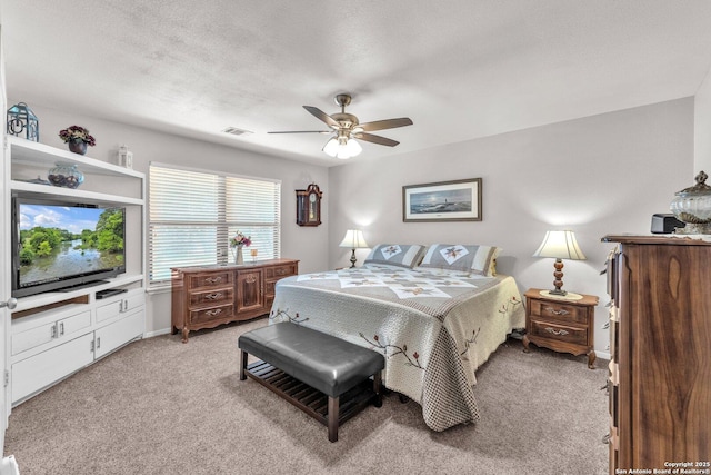 bedroom featuring a ceiling fan, light colored carpet, visible vents, and a textured ceiling