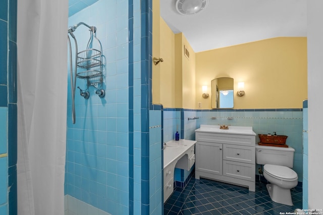 full bath with tile patterned flooring, a tile shower, tile walls, and wainscoting