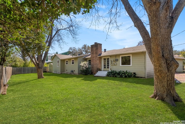 rear view of house featuring entry steps, fence, a chimney, and a lawn