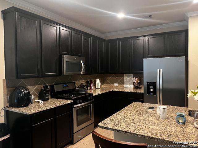 kitchen featuring ornamental molding, light stone countertops, stainless steel appliances, dark cabinetry, and backsplash