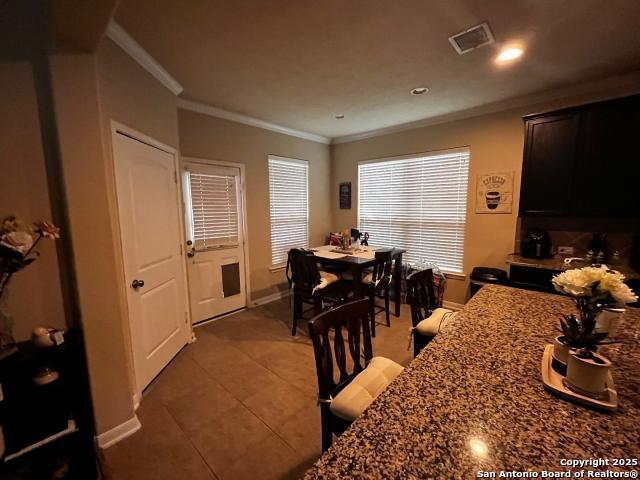 dining area with light tile patterned floors, visible vents, baseboards, and crown molding