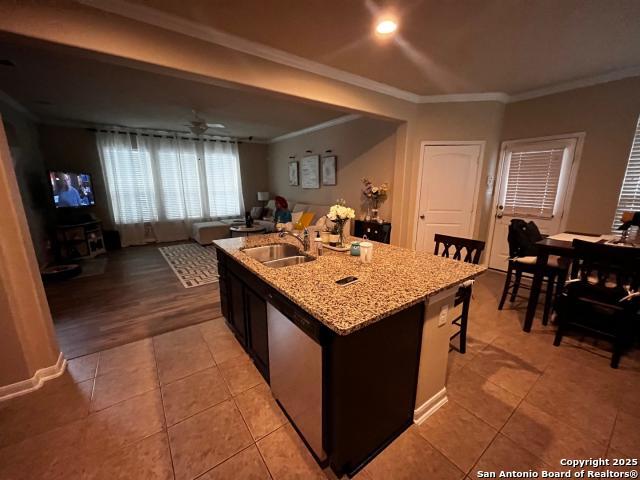 kitchen featuring light tile patterned floors, a ceiling fan, dishwasher, a kitchen island with sink, and a sink