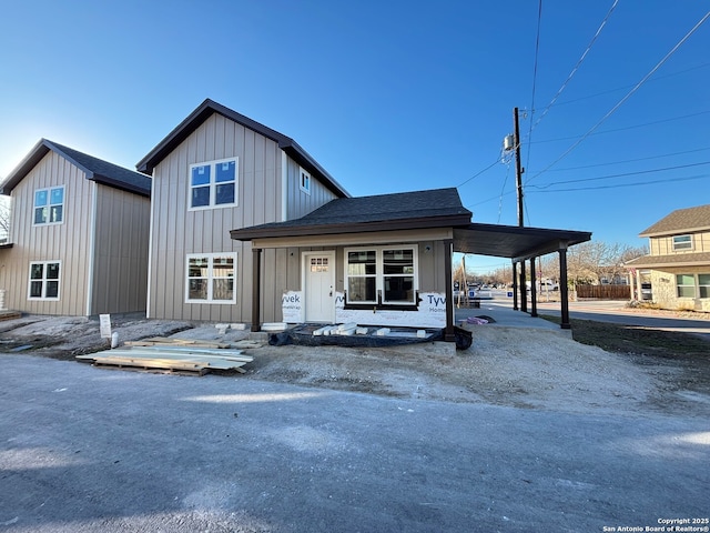 view of front of home with driveway, an attached carport, roof with shingles, covered porch, and board and batten siding