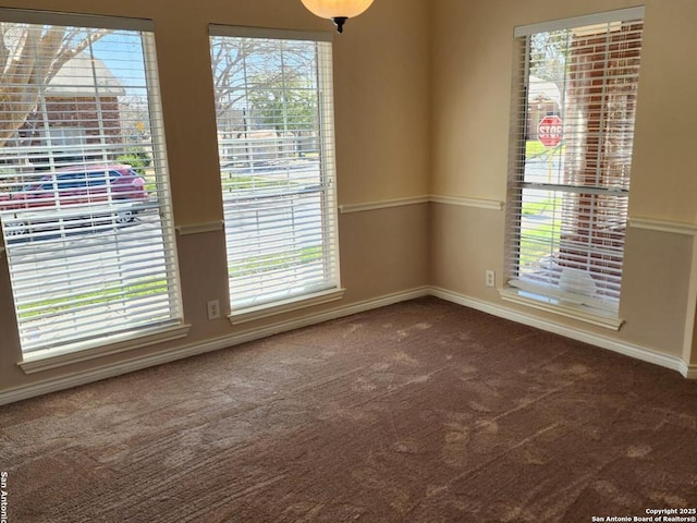 unfurnished room with dark colored carpet, a wealth of natural light, and baseboards