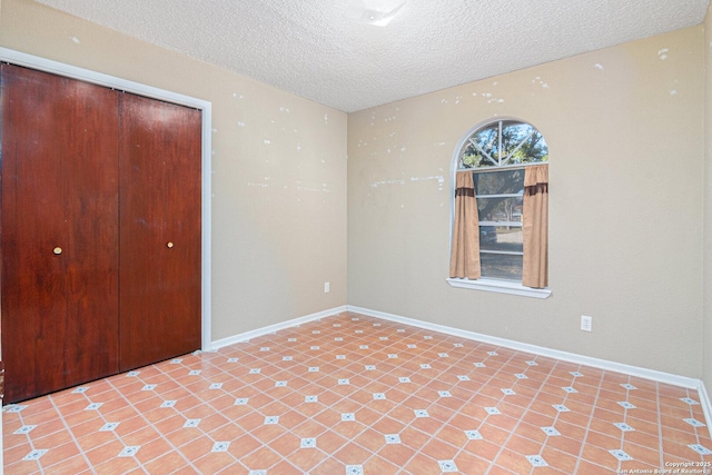 spare room featuring a textured ceiling, light tile patterned flooring, and baseboards