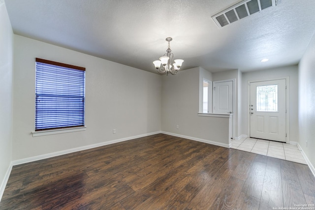 entrance foyer with baseboards, visible vents, wood finished floors, an inviting chandelier, and a textured ceiling