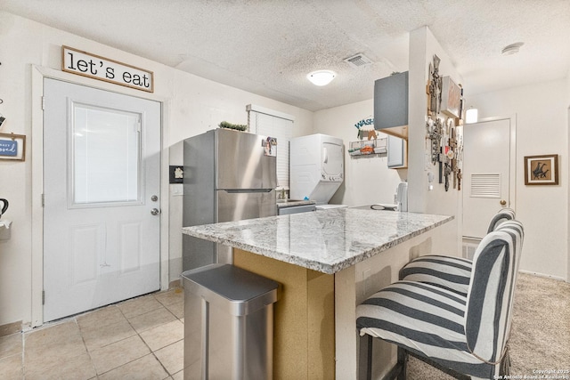 kitchen with stacked washer / dryer, freestanding refrigerator, a textured ceiling, and light stone countertops